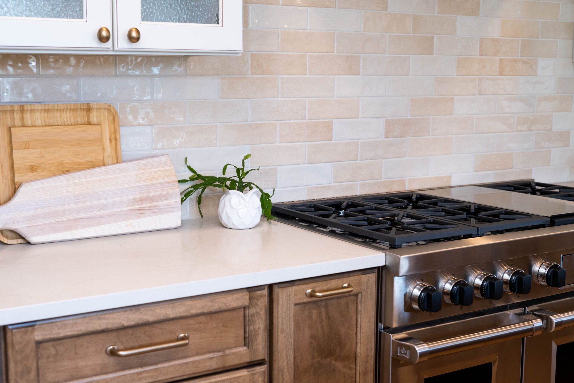 Kitchen with light countertops, stove, wood cabinets, white backsplash, and decorative cutting boards.