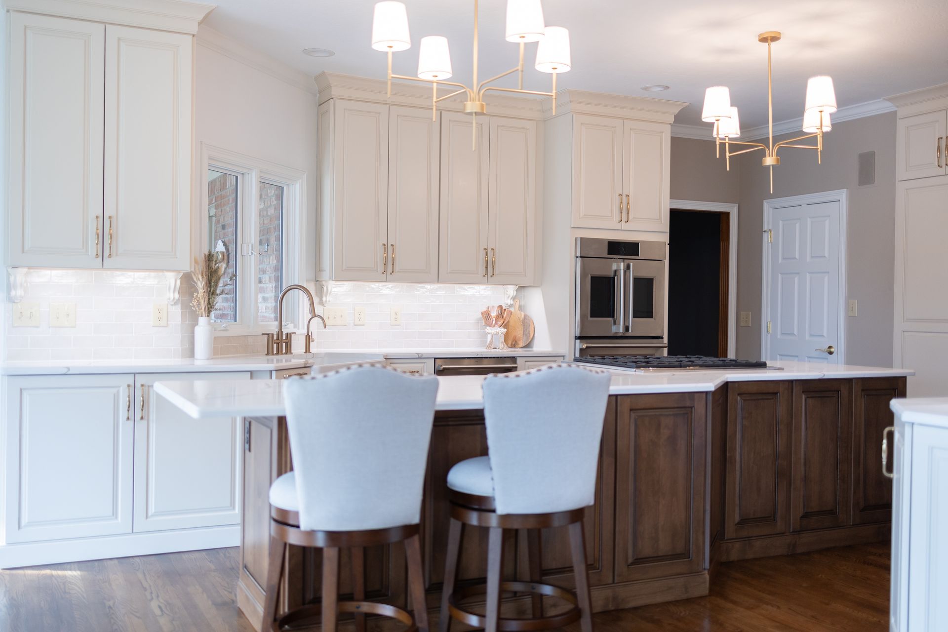 Bright white kitchen with dark wood island, barstools, pendant lights, and stainless steel appliances