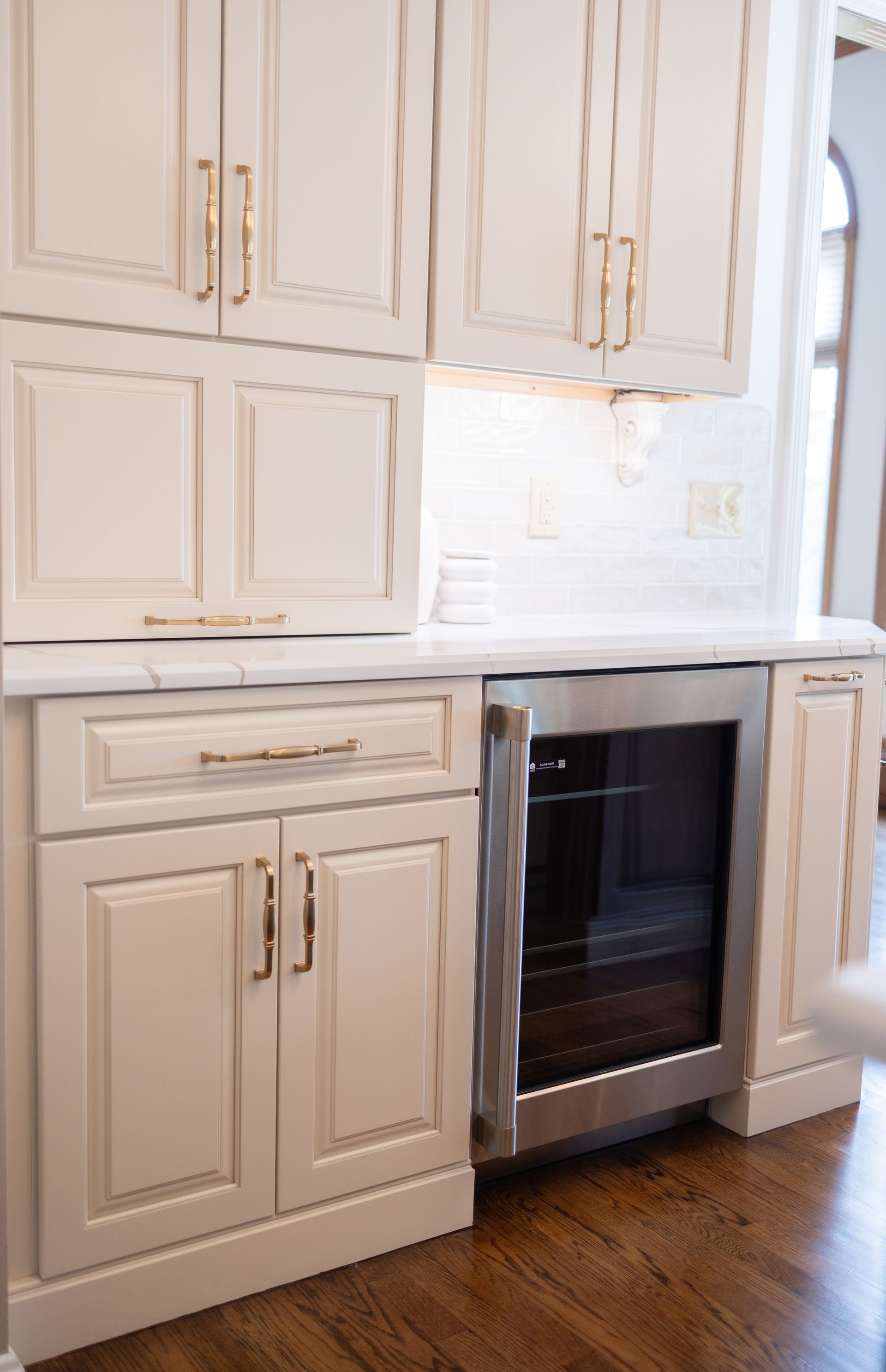 Cream-colored kitchen cabinets with a built-in stainless steel oven and hardwood floor by a bright window