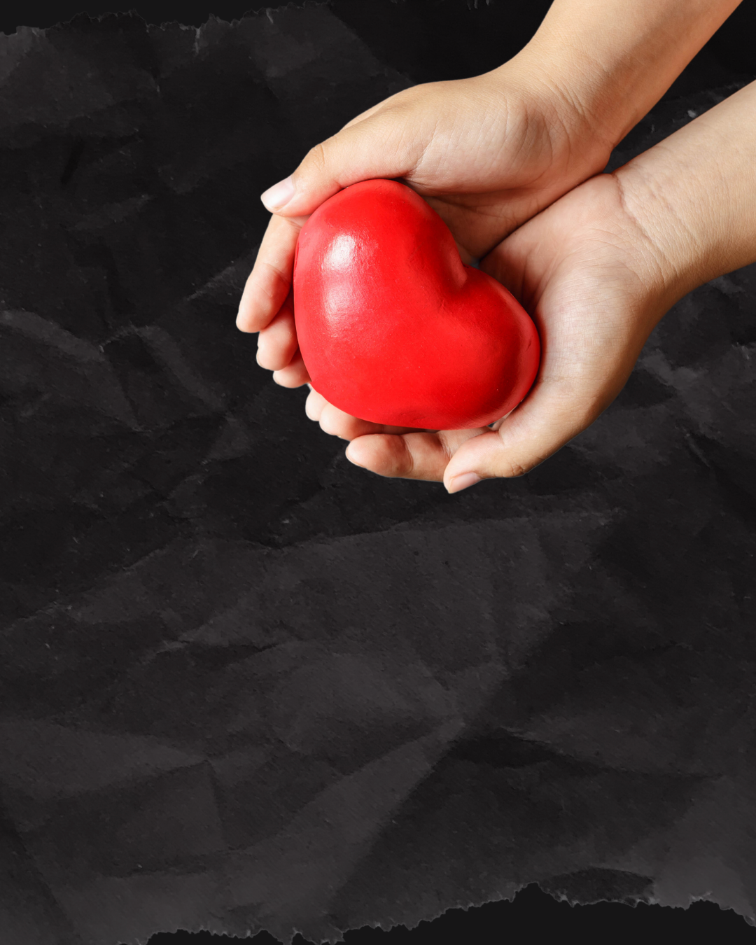 A person is holding a red heart in their hands