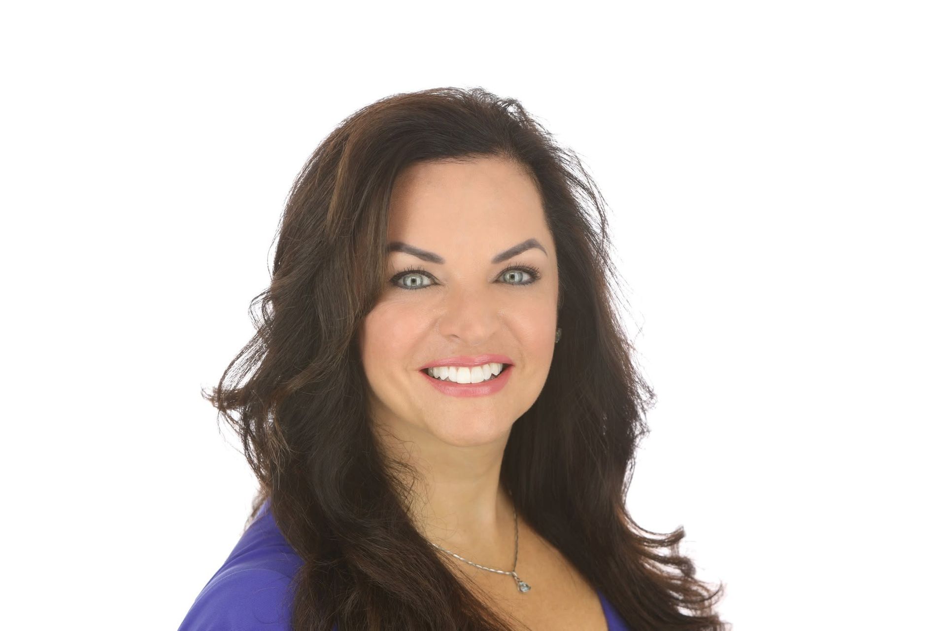 Woman with long brown hair smiles, wearing a blue top, against a white background.