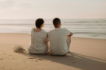 Couple sitting on a beach, looking at the ocean at sunset.