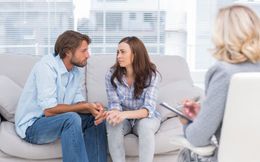 Couple in therapy session, talking to a therapist who's taking notes.