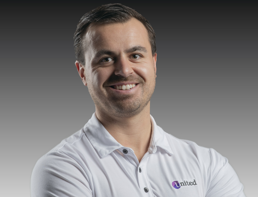 A man in a white shirt is smiling with his arms crossed.