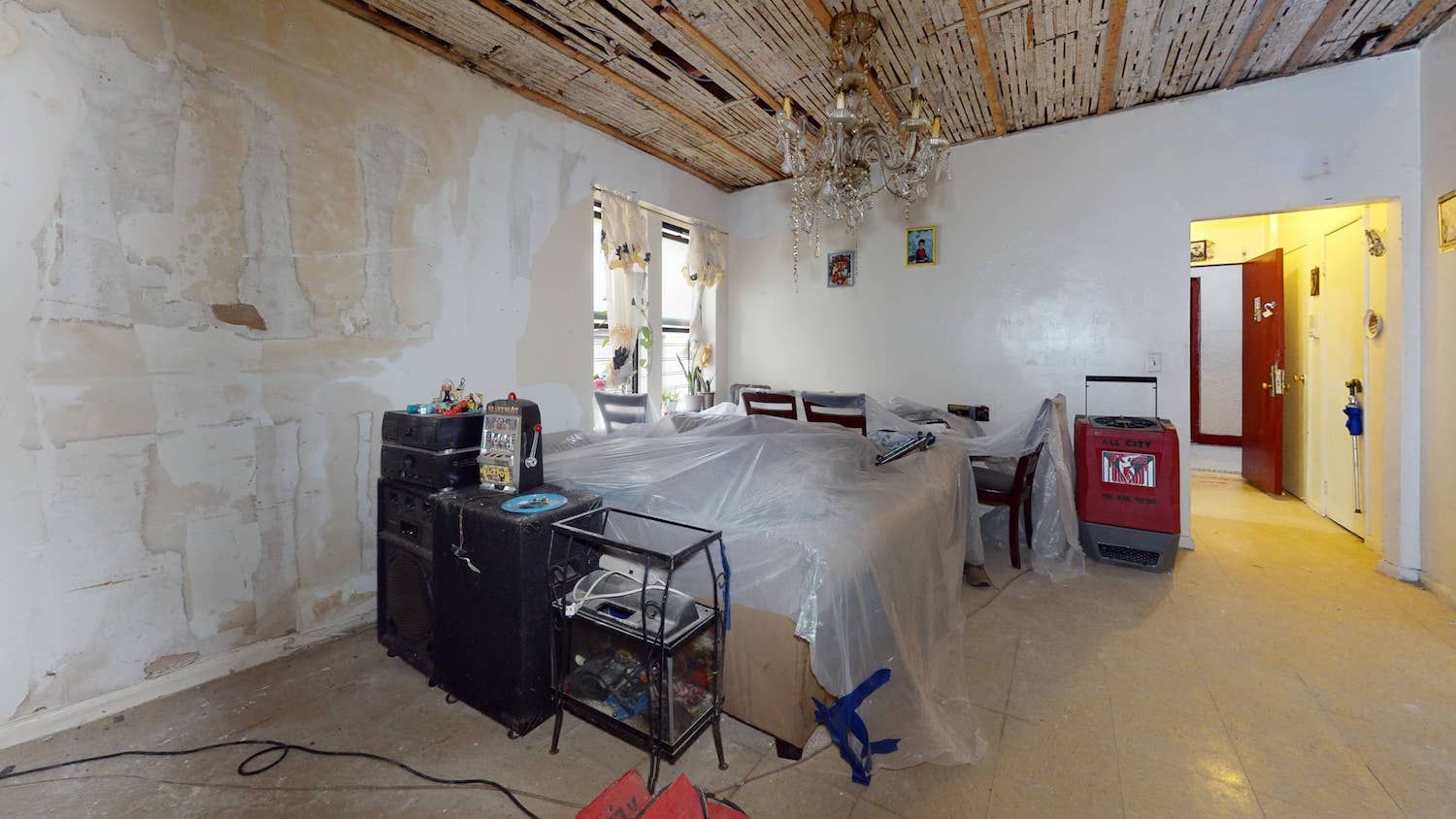 A room with a bed , a shelf , a vacuum cleaner and a chandelier.