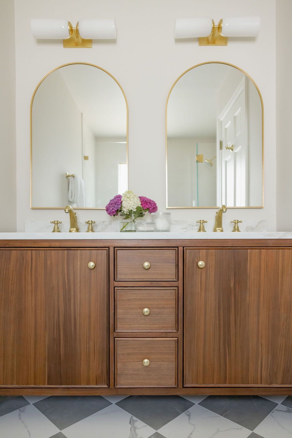 Bathroom with two arched mirrors, gold accents, walnut cabinets, and marble countertop.