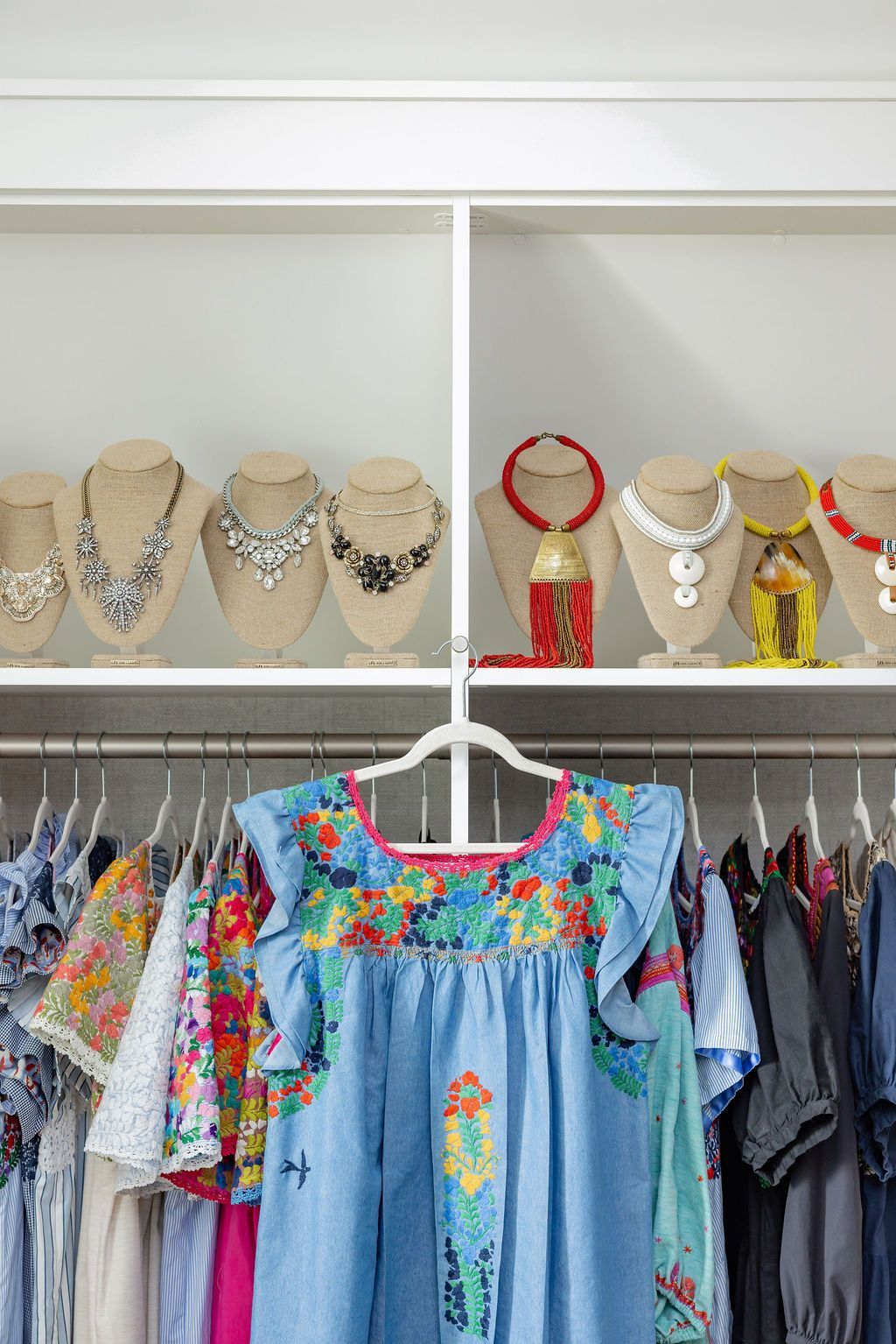 Clothing rack with dresses and shelf of necklaces in a white closet.