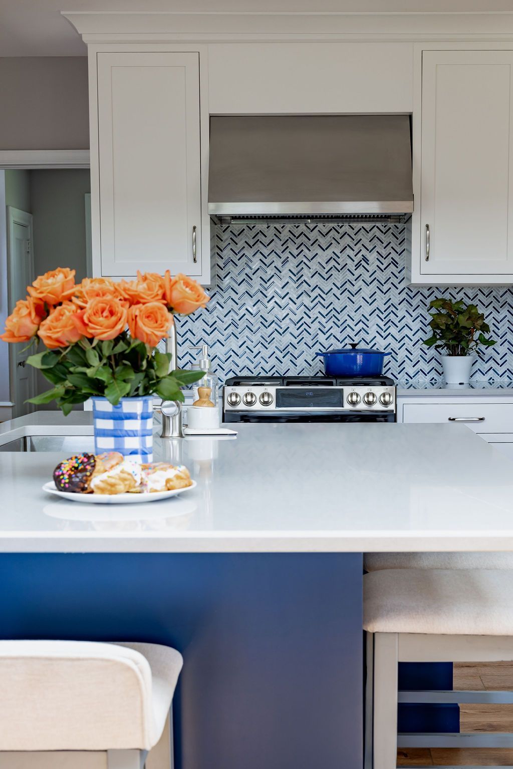 Kitchen island with flowers, pastries, and blue cabinets. White countertops and backsplash with stainless steel appliances.