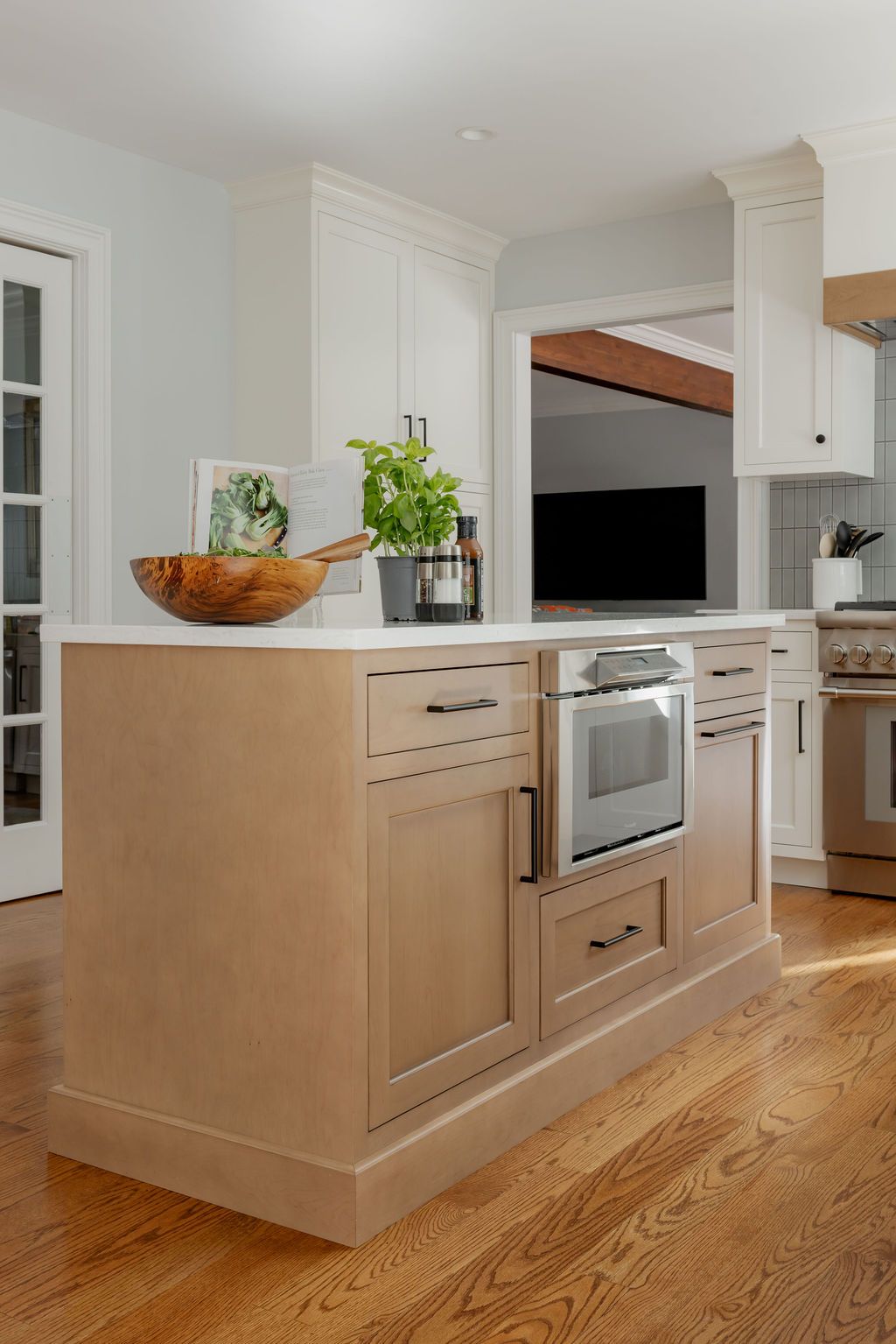 Kitchen island with built-in oven and drawers. Beige cabinets, white countertop, and hardwood floor.