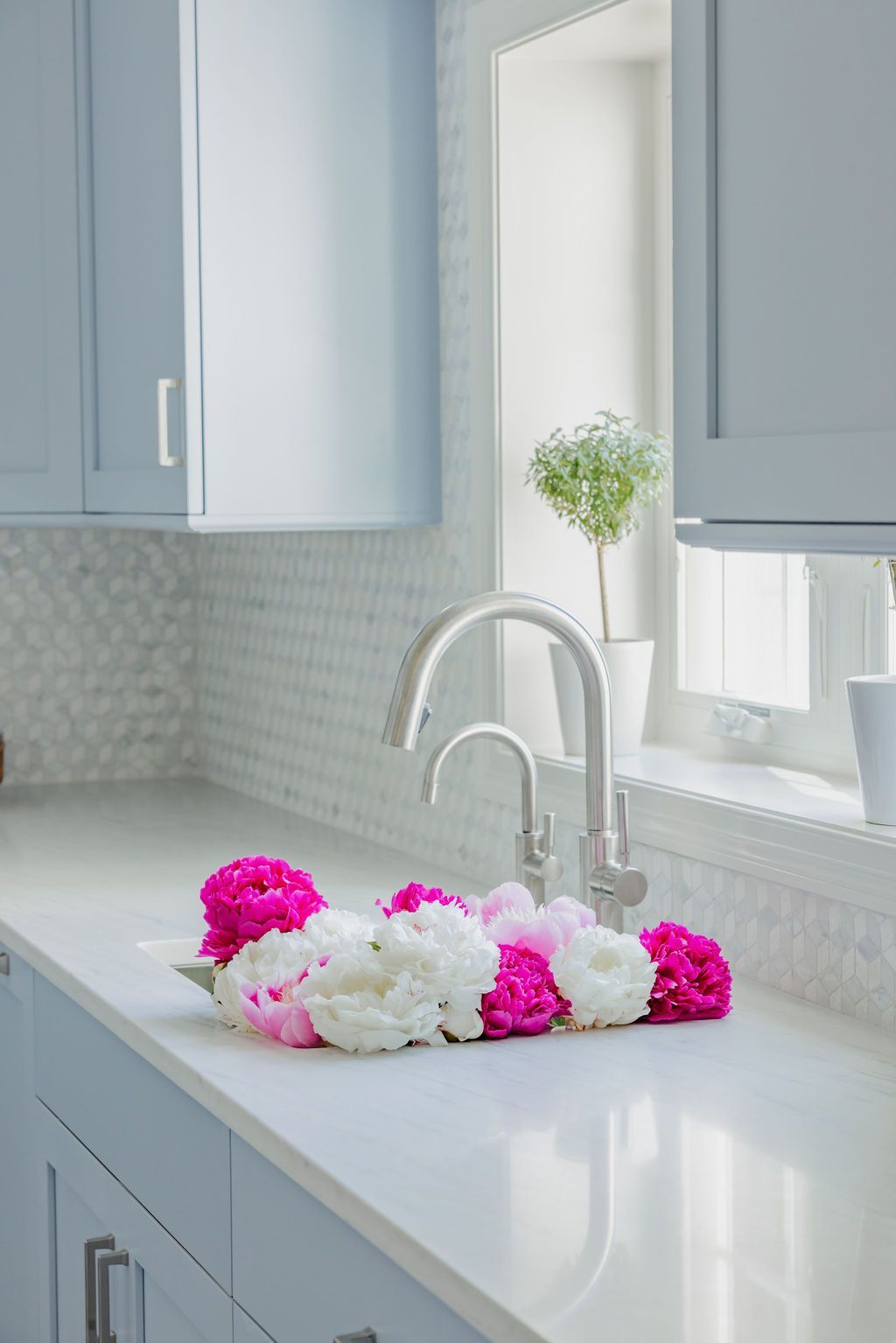 Kitchen with blue cabinets, white countertops, and peonies near the faucet.