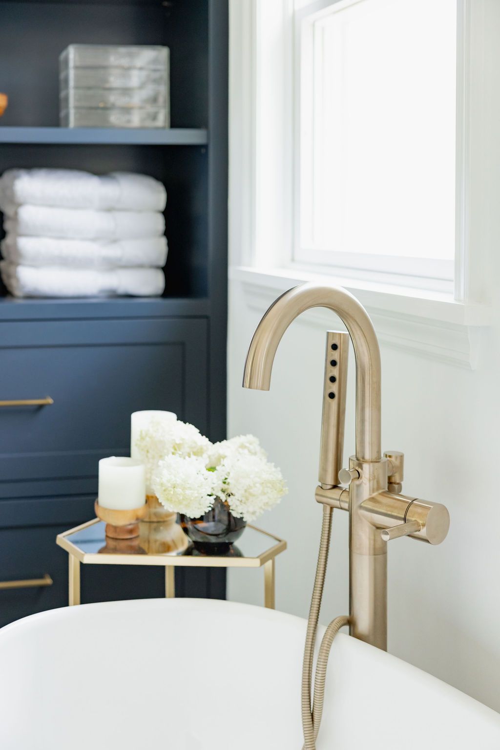 A bathroom with a freestanding tub, gold faucet, and blue storage cabinet.