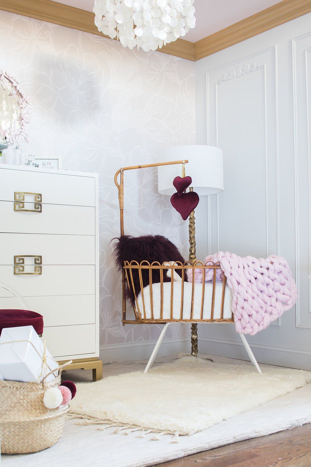 Baby crib in nursery with rug, dresser, and heart mobile.