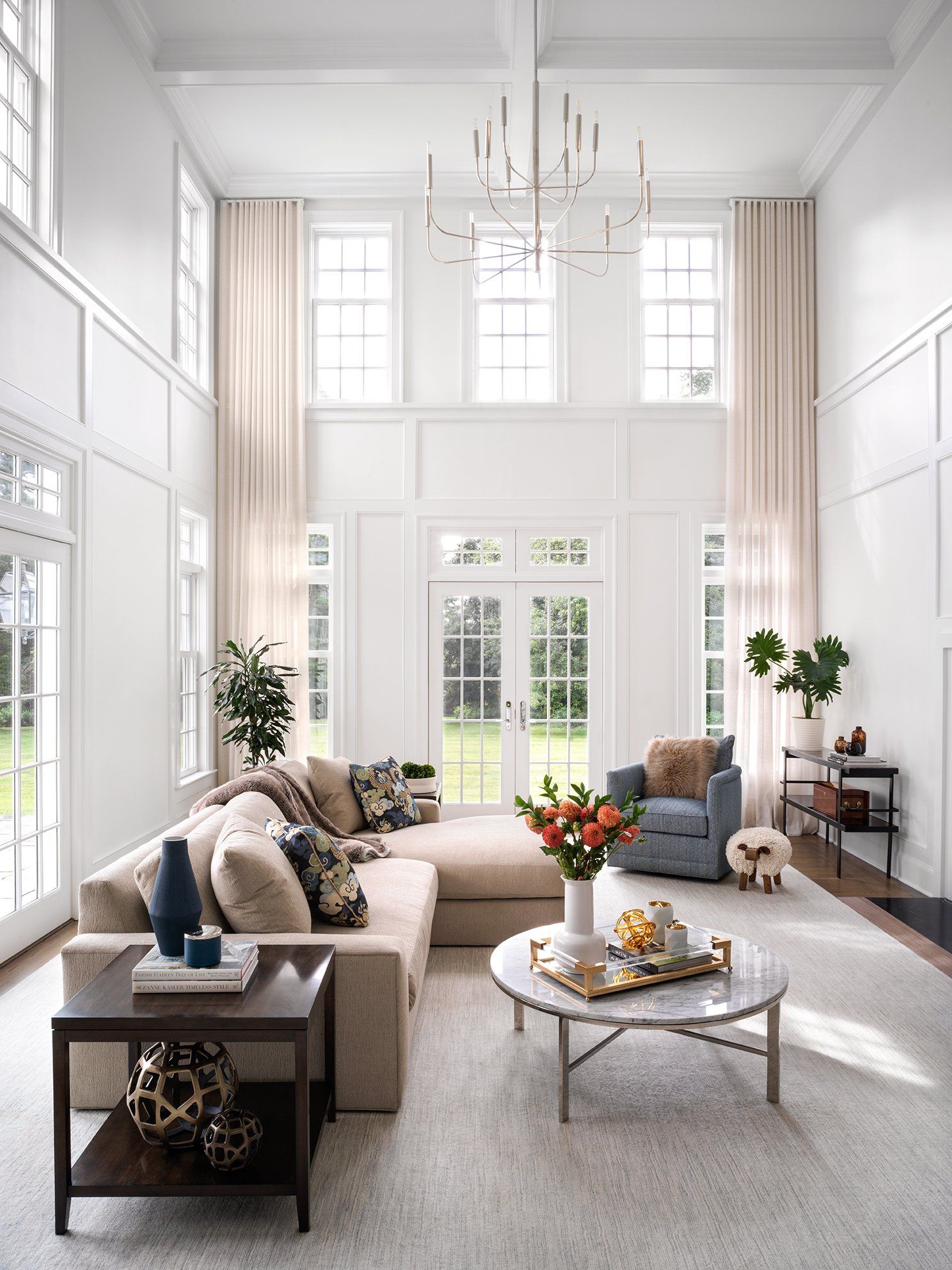 Spacious living room with high ceilings, large windows, and neutral color scheme. Furnished with sectional sofa and arm chair.