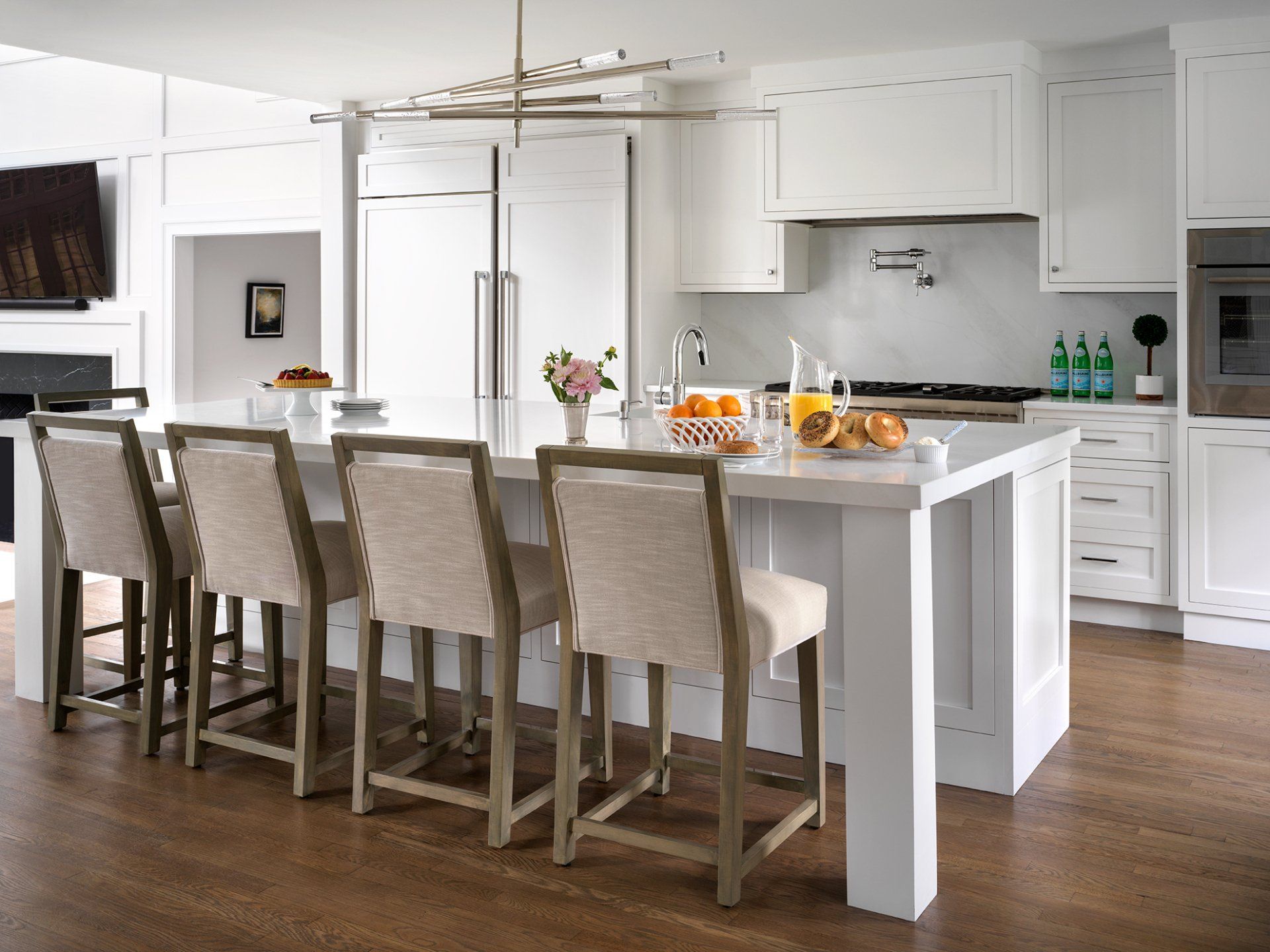 White kitchen with island, bar stools, and modern appliances. Wooden floor.