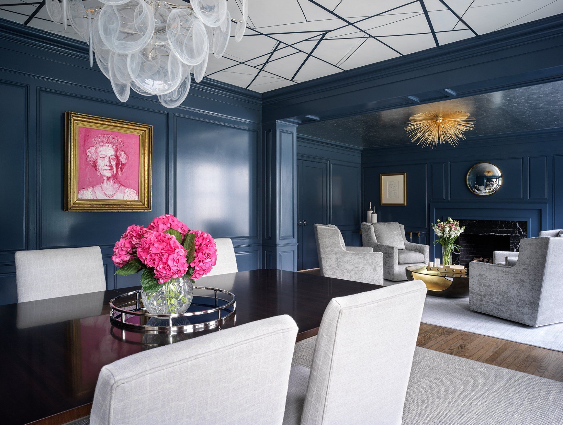Elegant blue dining room with dark wood table, pink floral arrangement, and white chairs.
