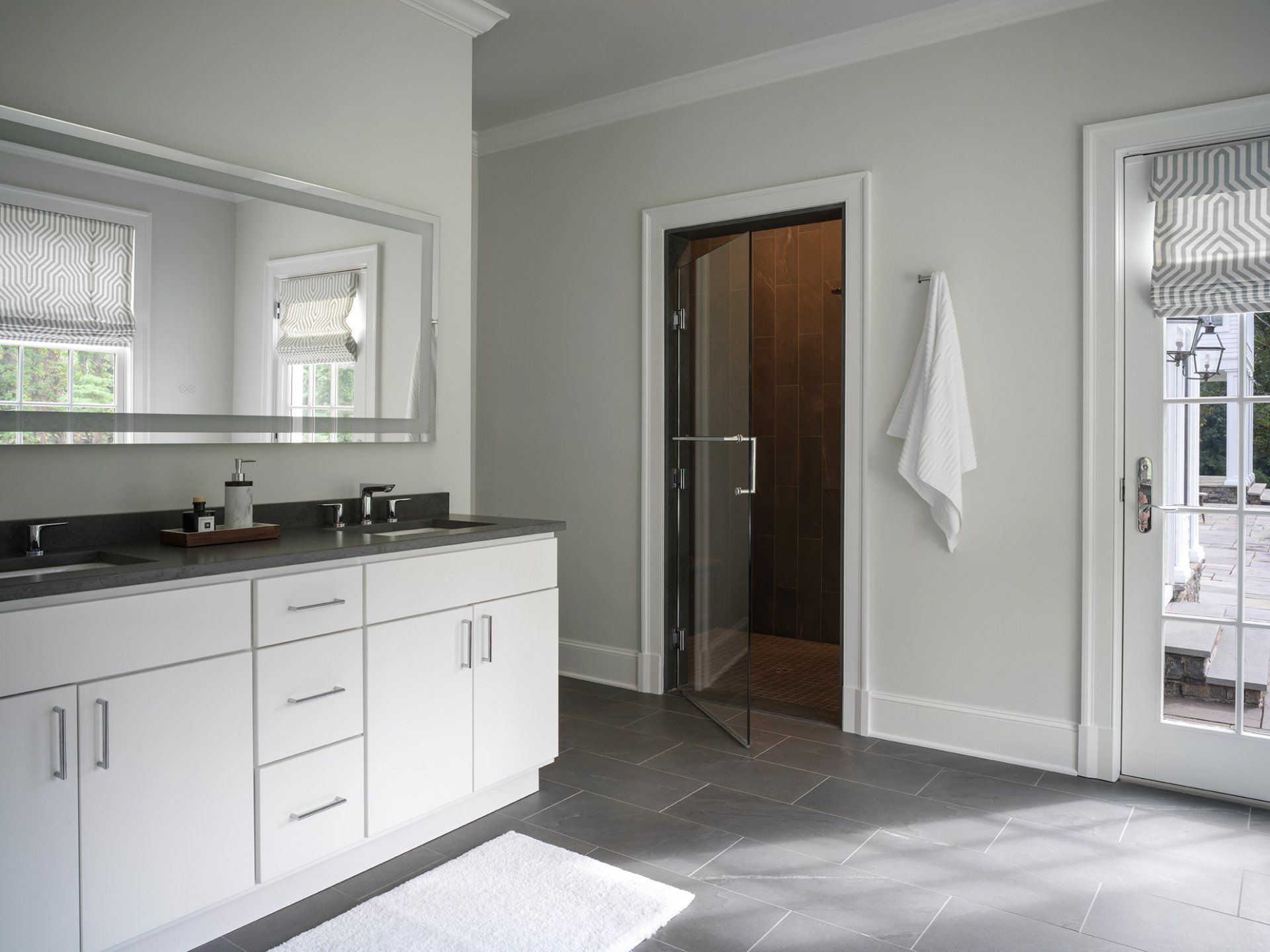 Bathroom with white cabinets, large mirror, gray tile floor, and glass shower door.
