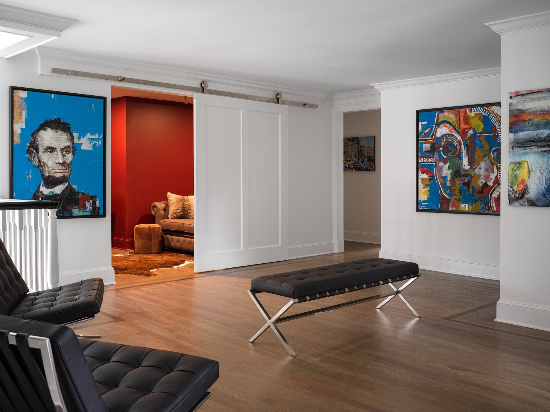 Modern art gallery with colorful paintings, a black bench, and a sliding door.