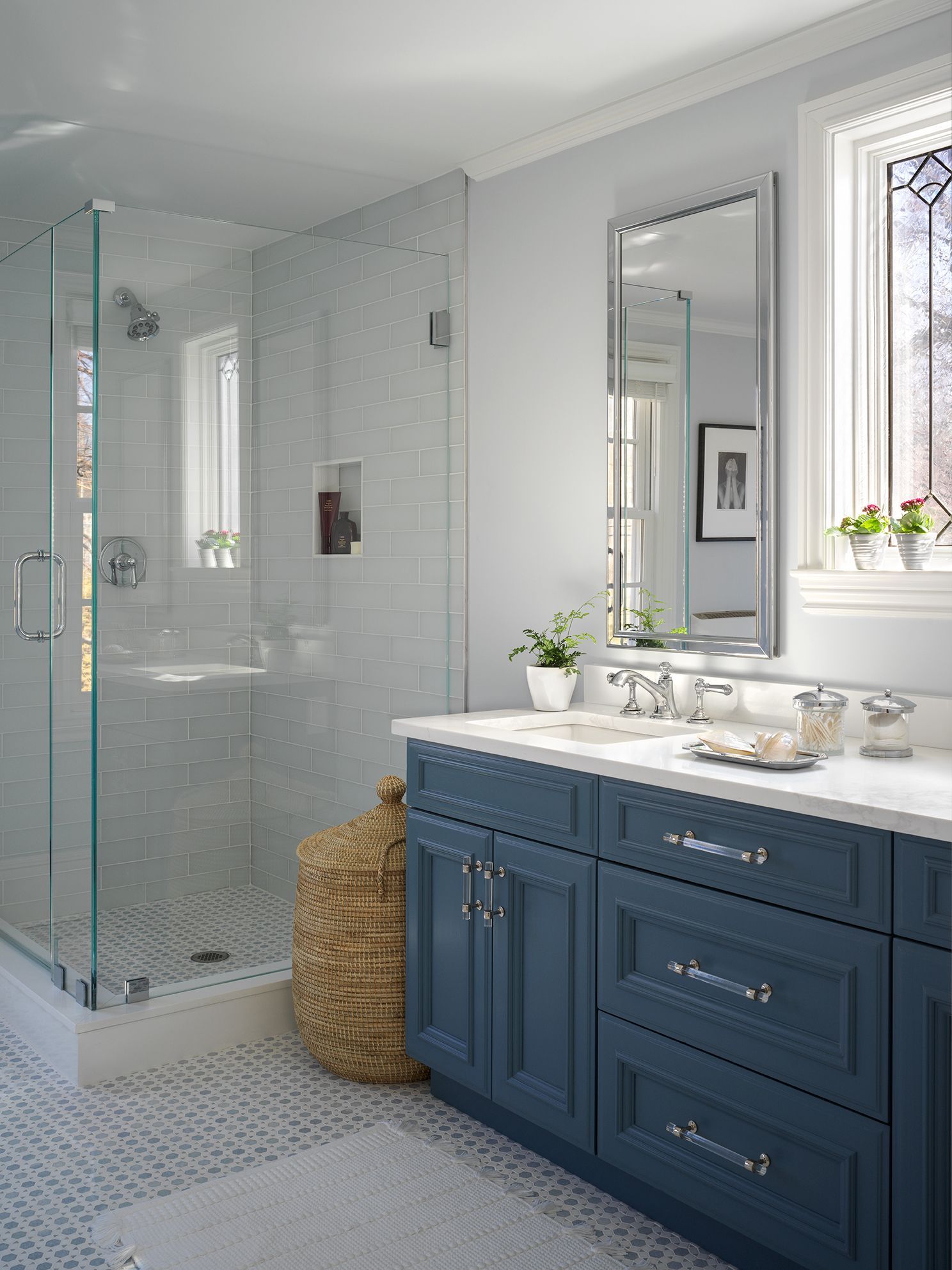 Bathroom with blue vanity, glass shower, and patterned floor.