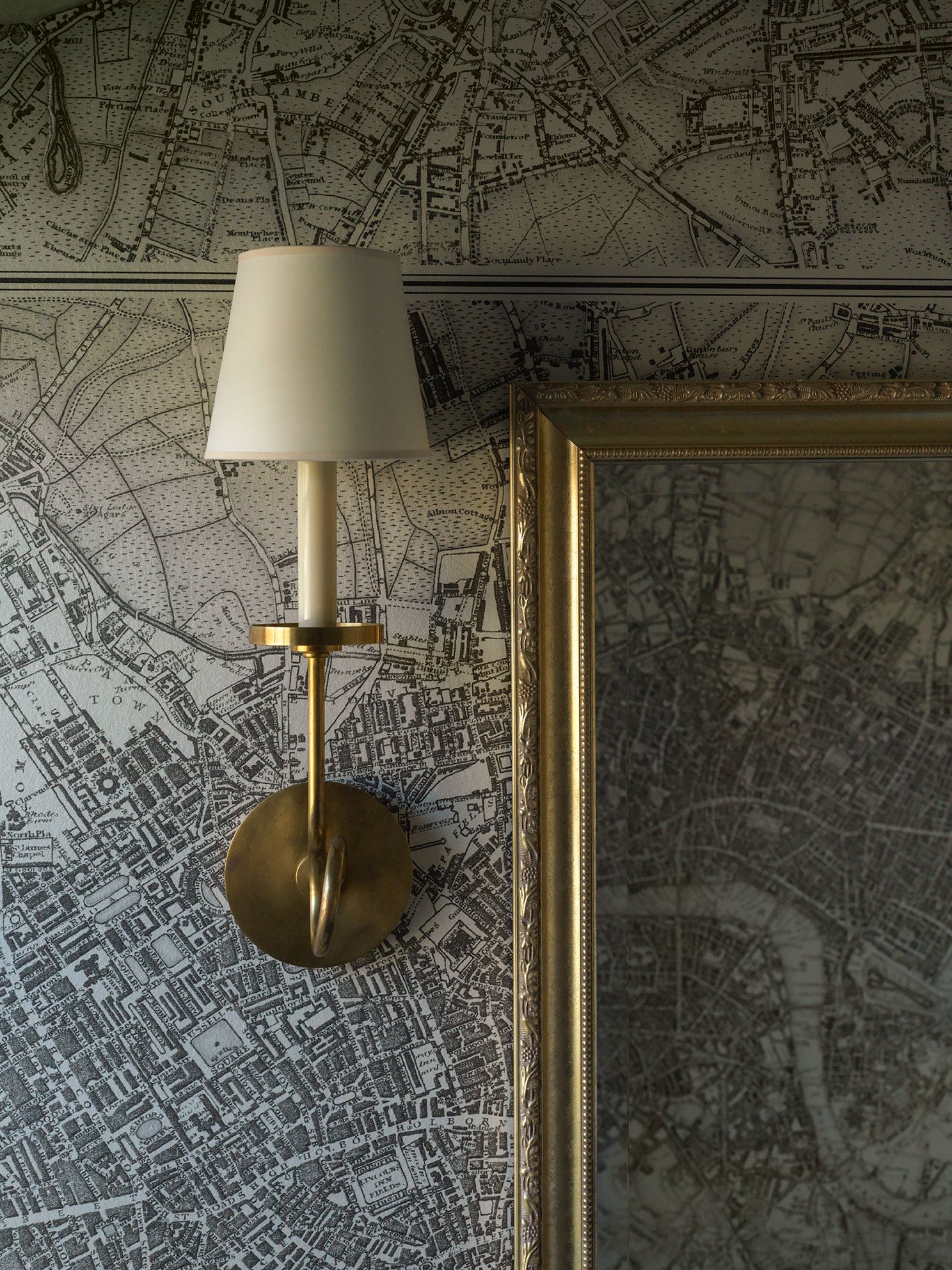 Wall-mounted lamp and gold-framed art against a map-patterned wallpaper.