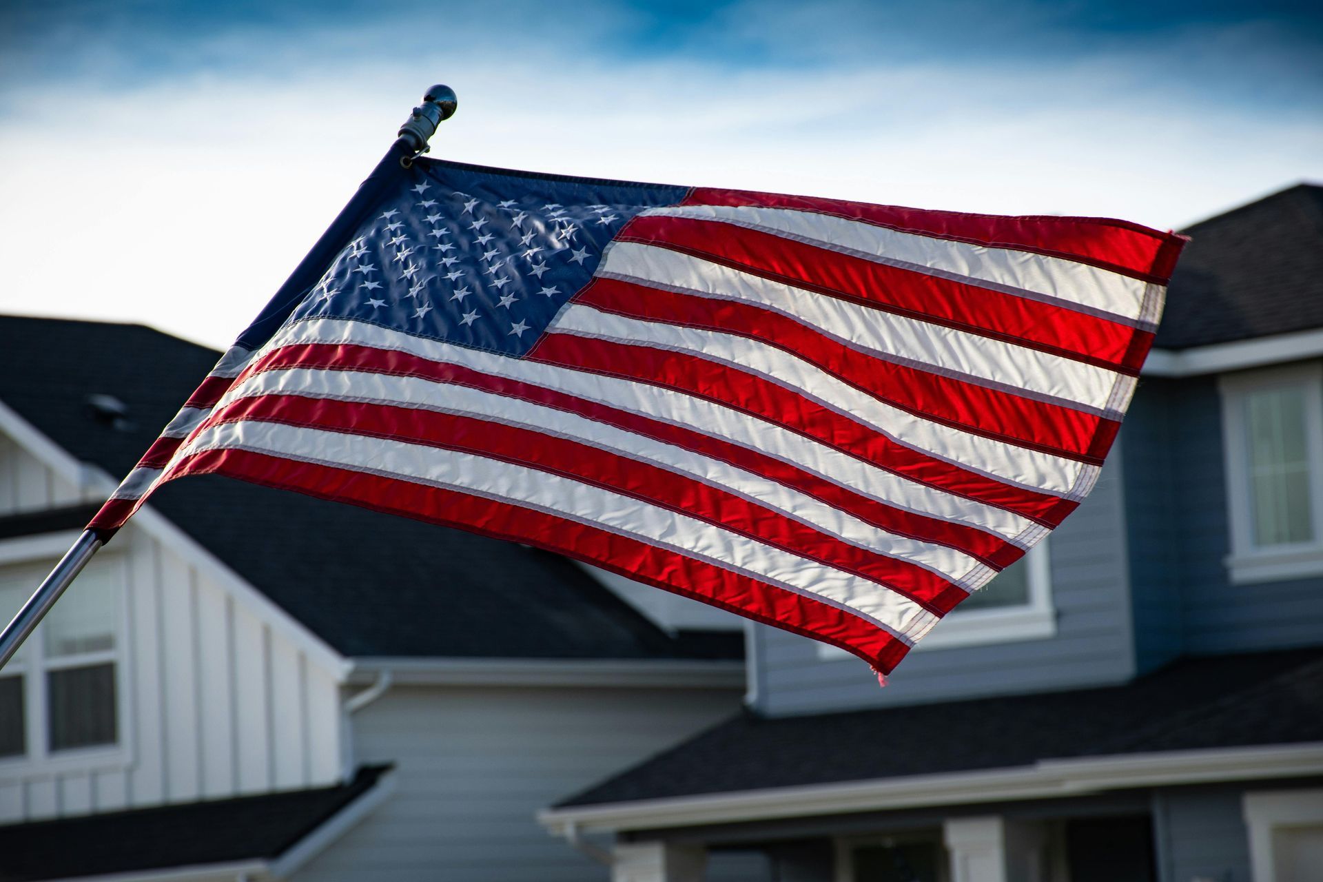 American flag waving in front of a blue and white house under a blue sky.