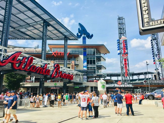 Crowd outside Atlanta Braves stadium entrance with red signage and a blue baseball player statue