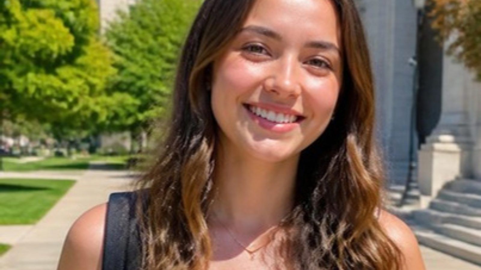 Smiling college student with long wavy hair outside a campus building on a sunny day