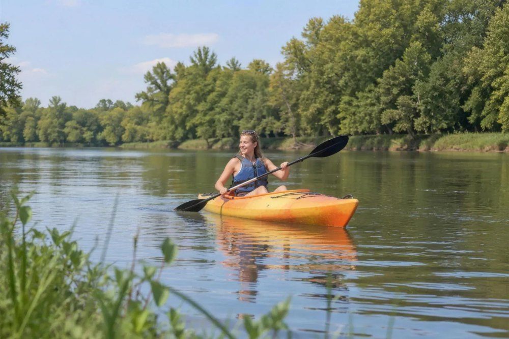 Young woman smiling as she kayaks on a calm, tree-lined river on a sunny day