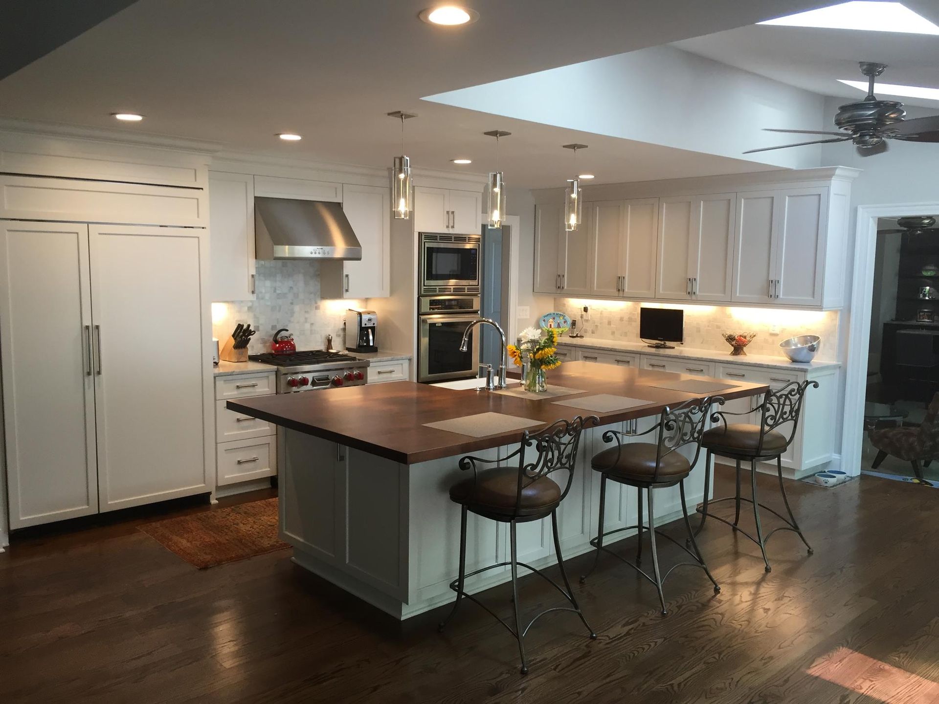 White kitchen with large island and seating, stainless steel appliances, and overhead lighting.