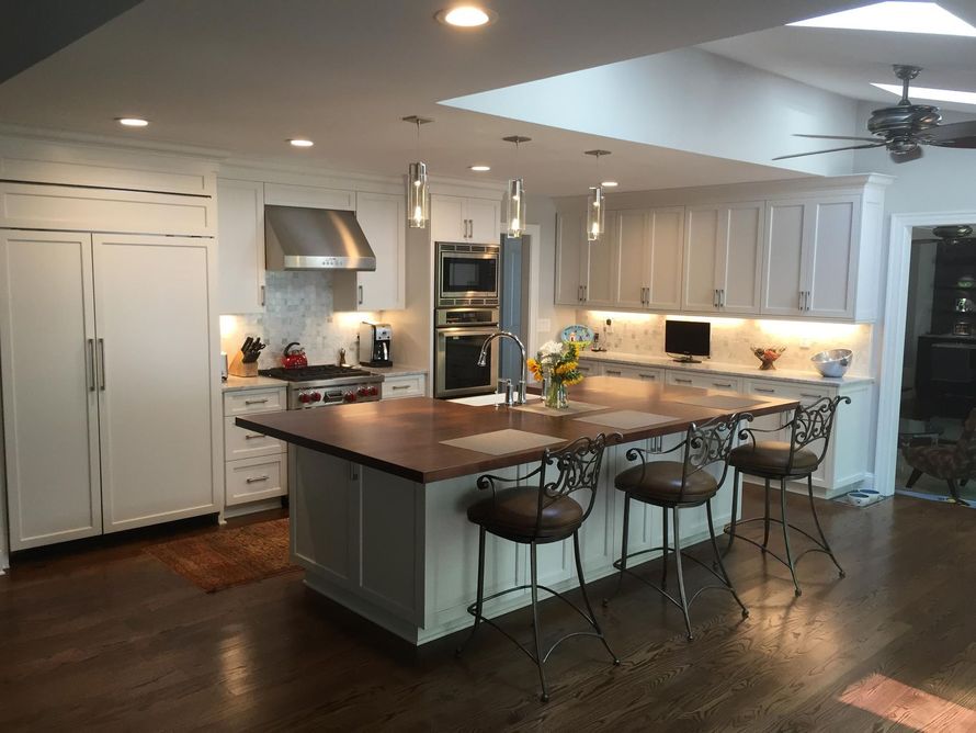 A bright white kitchen with a large island, stainless steel appliances, and bar stools.