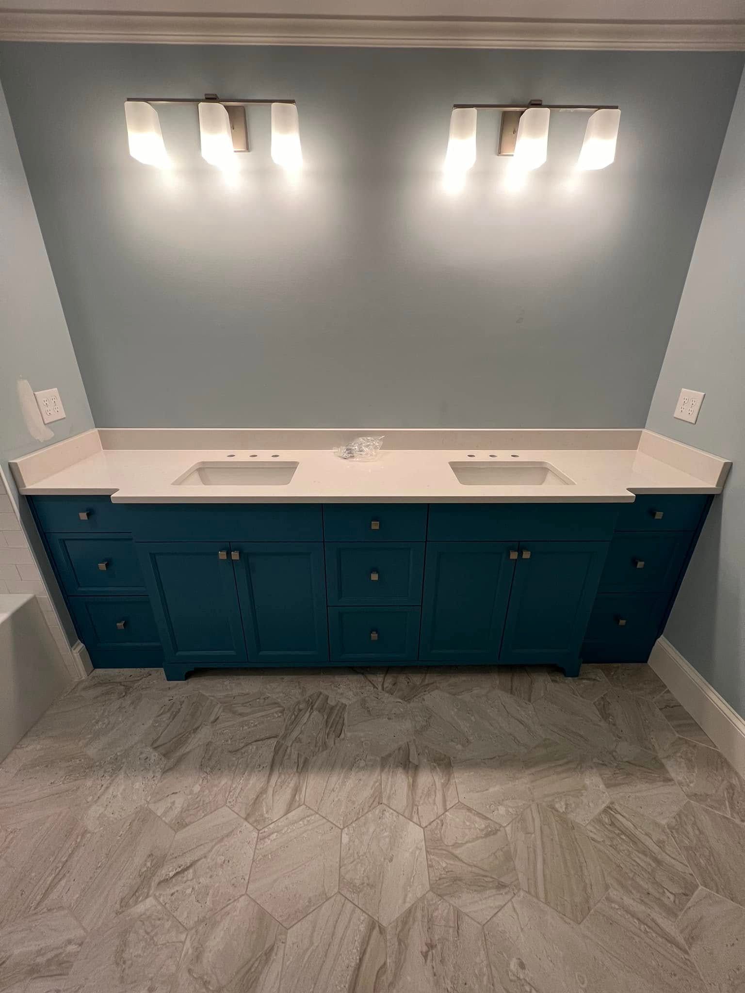 Teal double vanity with white countertop and gray tiled floor in a blue-walled bathroom, lit by two sconces.