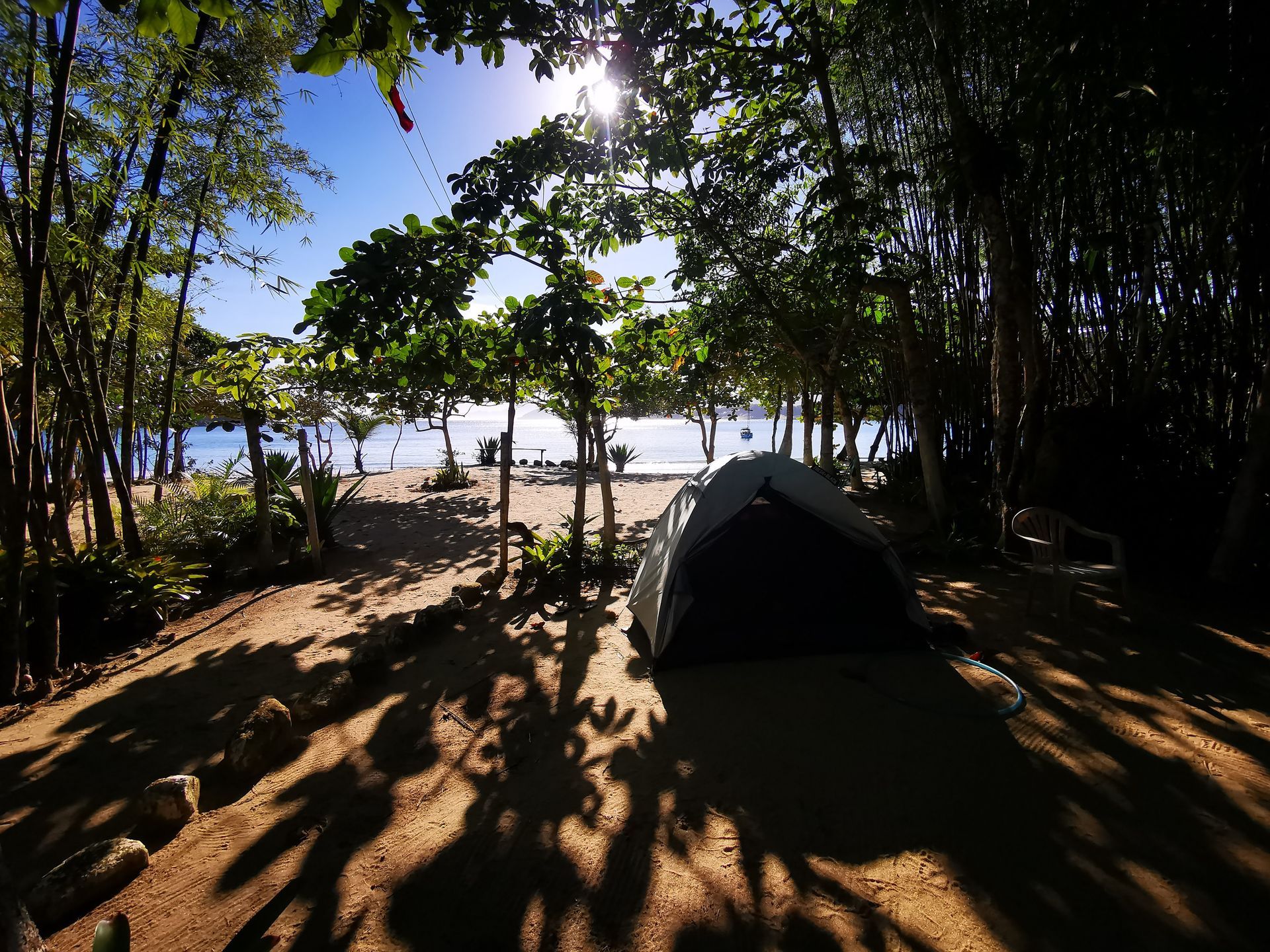 Peaceful camping site at Parnaioca, Ilha Grande, with a tent set up under the shade of tropical trees, overlooking a sandy beach and calm ocean waters in the background, creating a serene and natural setting perfect for outdoor enthusiasts