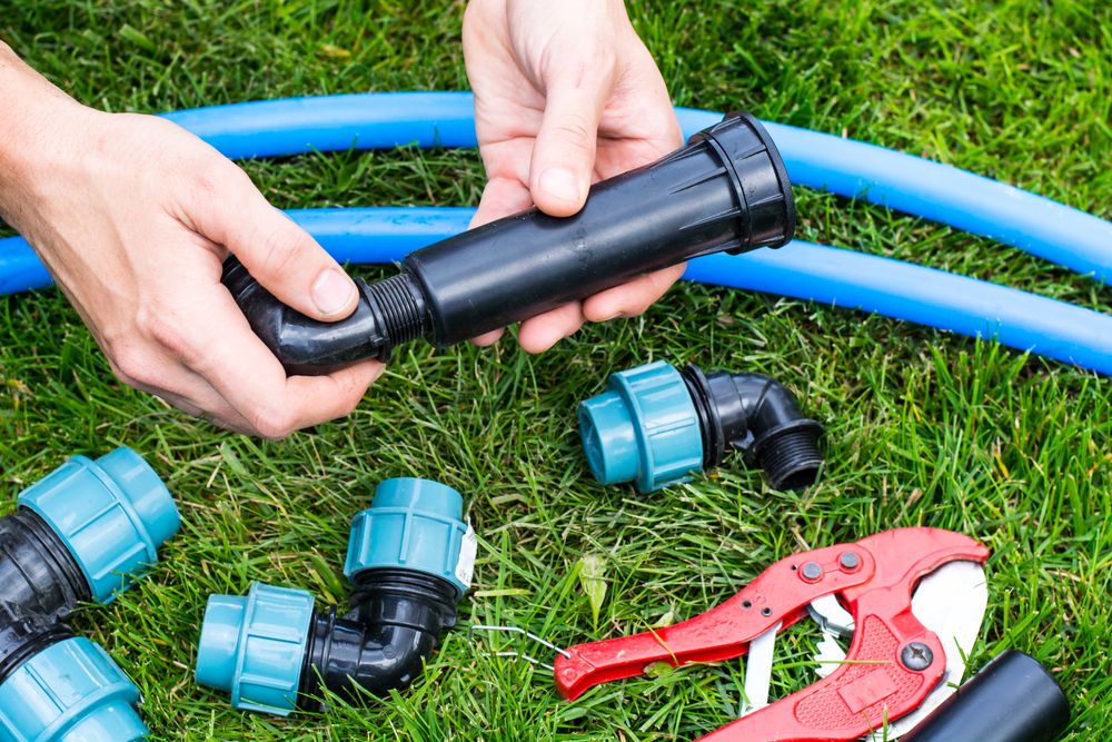 A Person is Fixing a Hose on the Grass With a Pair of Pliers — Sweeney's Pumps & Irrigation In Stroud, NSW