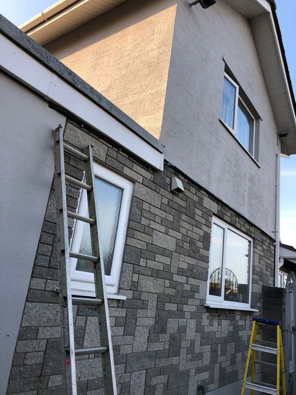 Ladder beside a house exterior with stone cladding and white upper walls under renovation.