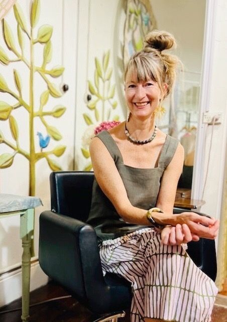 A woman is sitting in a chair with her hands folded and smiling.