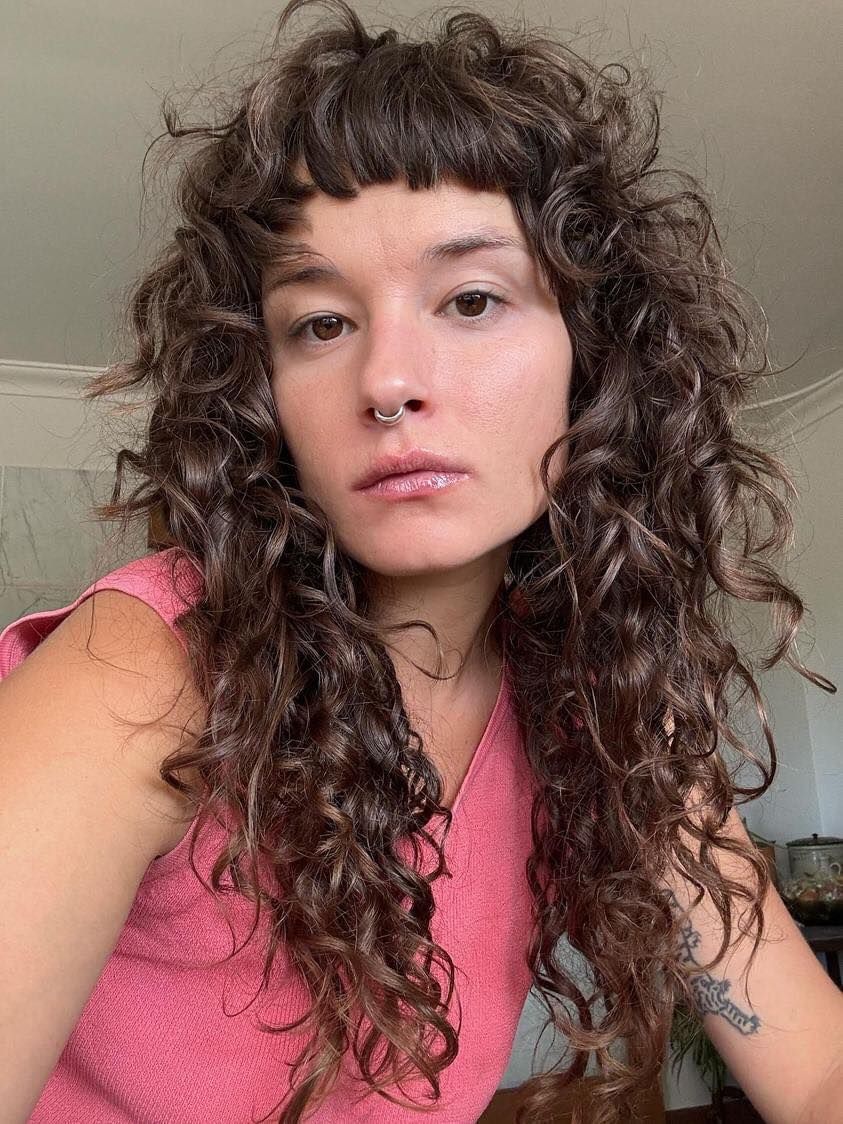 A woman with curly hair and a nose ring is taking a selfie.