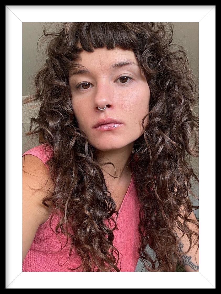 A woman with curly hair and a nose ring is taking a selfie.