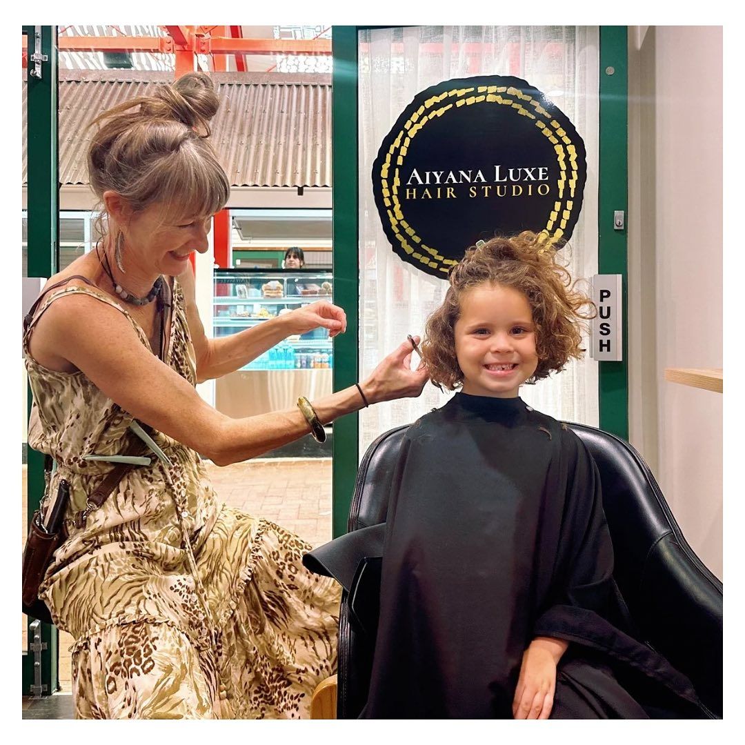 A woman is cutting a little girl 's hair at a hair studio