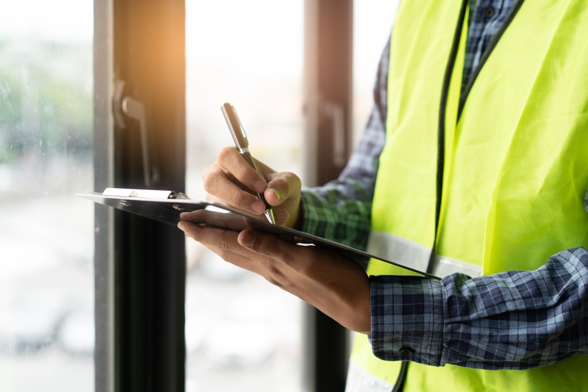 A man in a yellow vest is writing on a clipboard with a pen.