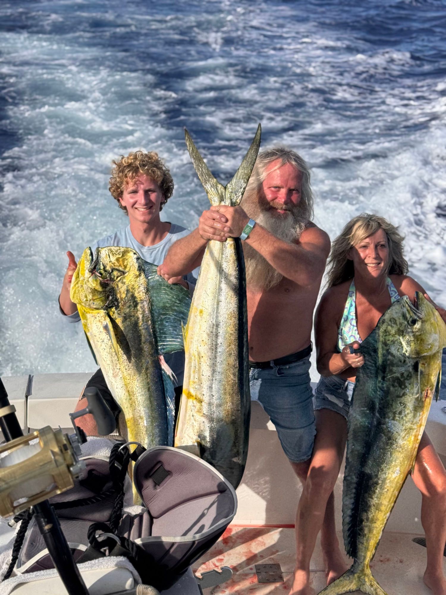 A man and two women holding large fish on a boat