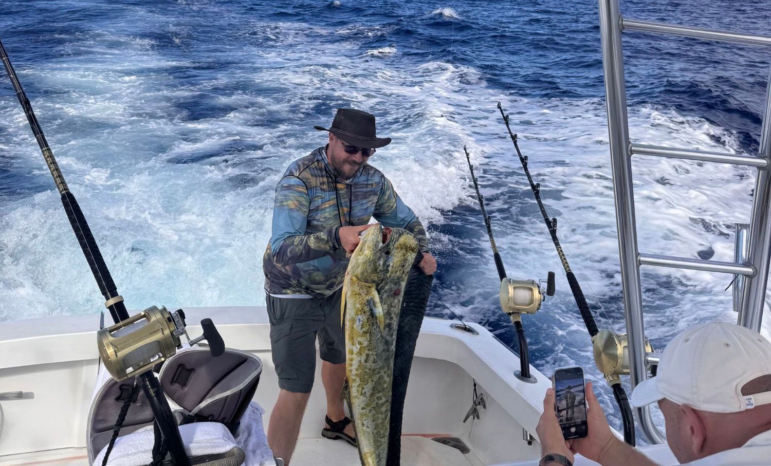 A man is standing on a boat holding a large fish.