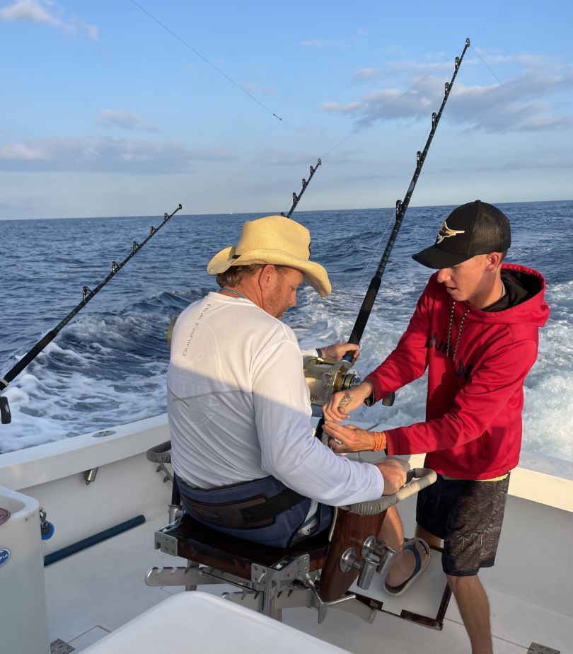 A man in a cowboy hat is fishing with a boy in a red hoodie