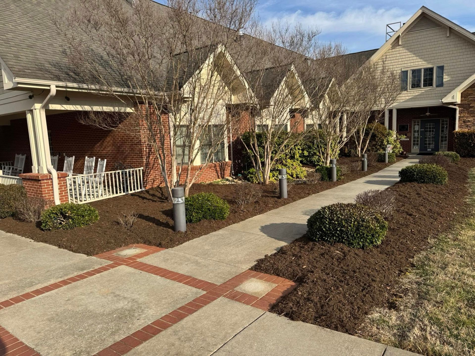 Suburban townhouse sidewalk and courtyard with brick paths, shrubs, and beige homes on a sunny day