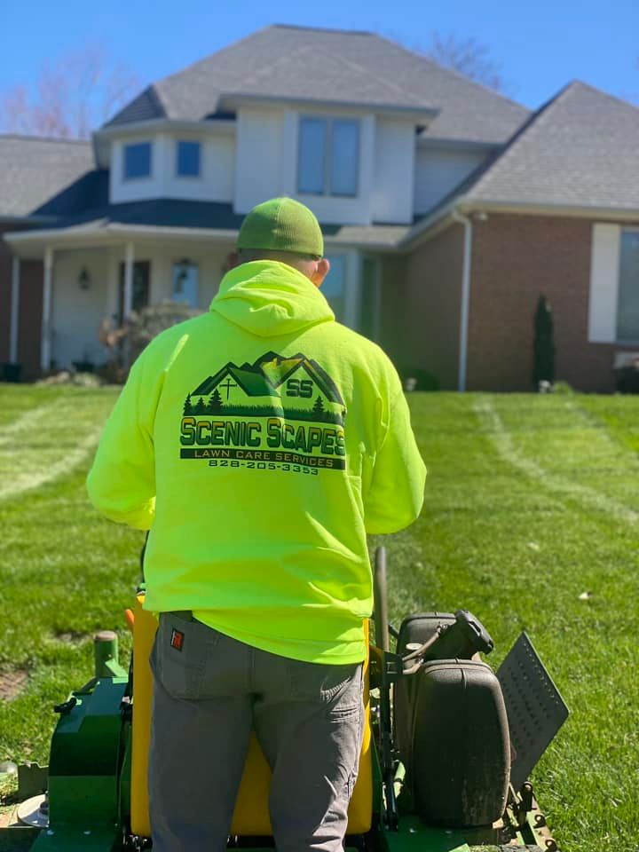 A person in a neon yellow hoodie works on a residential lawn, operating a riding mower in front of a suburban home.