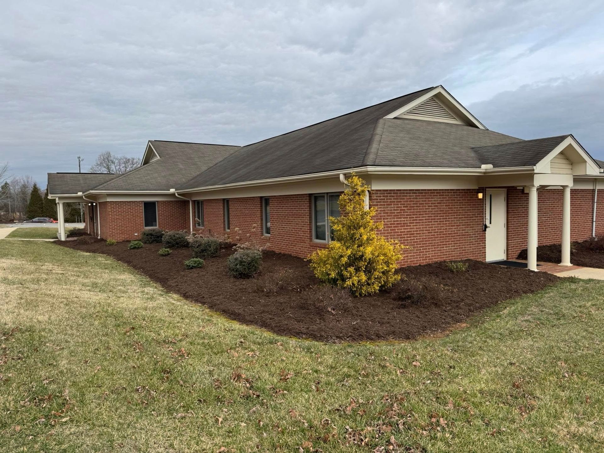 A single-story brick professional building with a shingled roof, landscaping, and a side entrance under a portico.