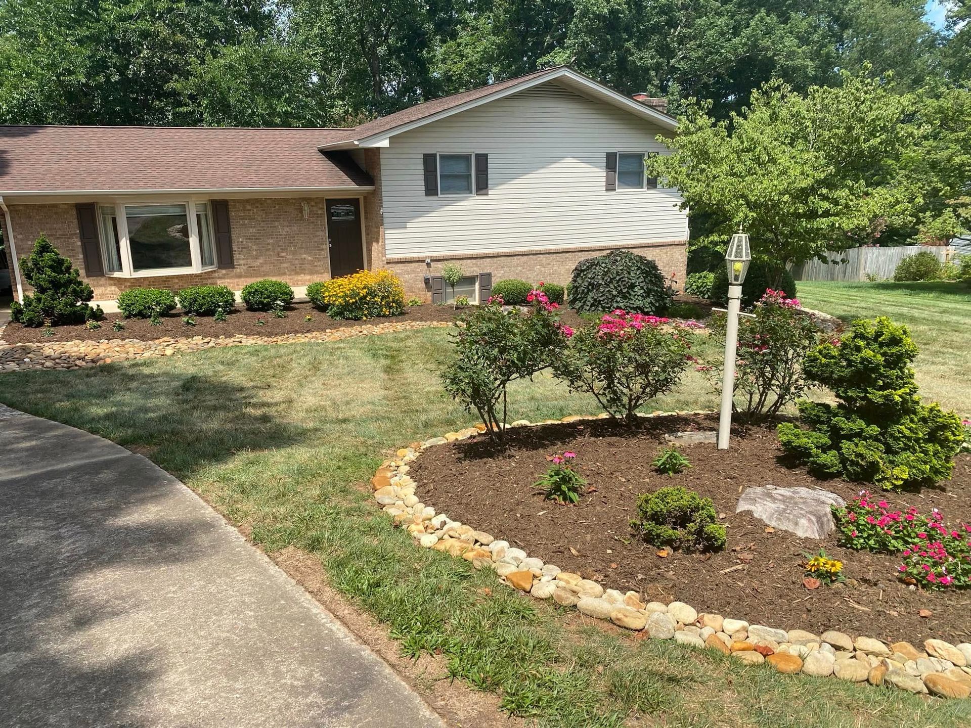 A split-level home with a stone and white siding exterior features a front yard with a rock-bordered landscaping bed.