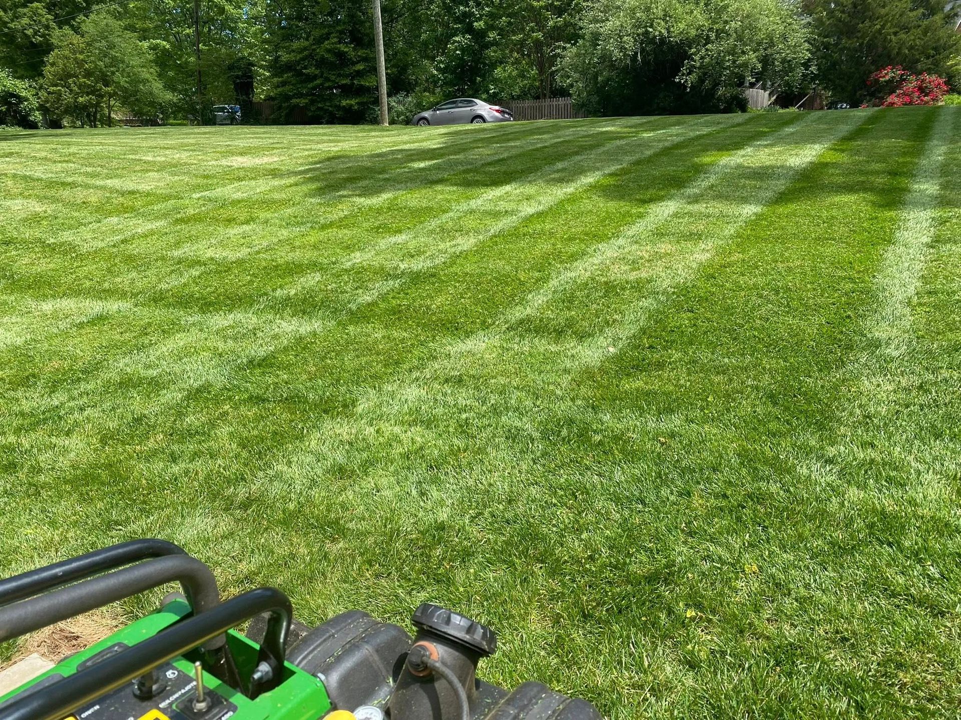 A view from a lawn mower showing a freshly cut, striped green lawn on a sunny day.