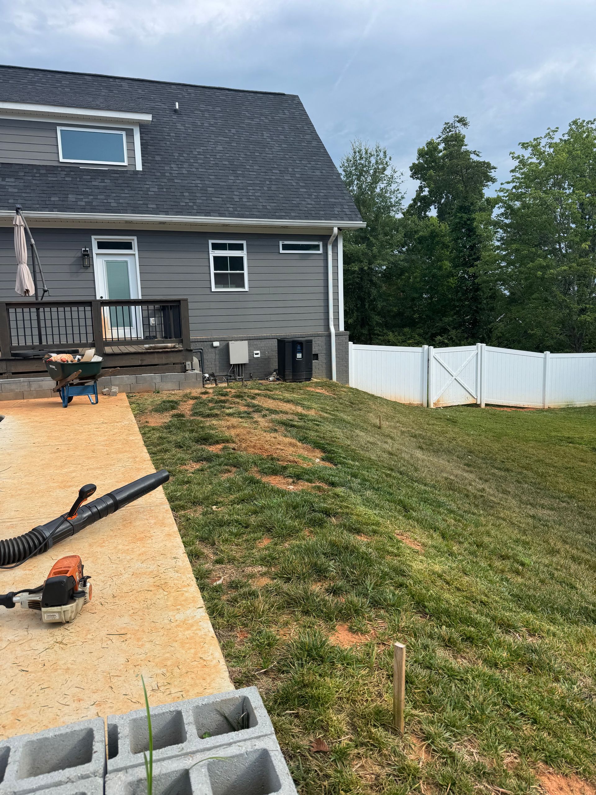 Partially built house with roof work, tools, and white fence beside grassy yard