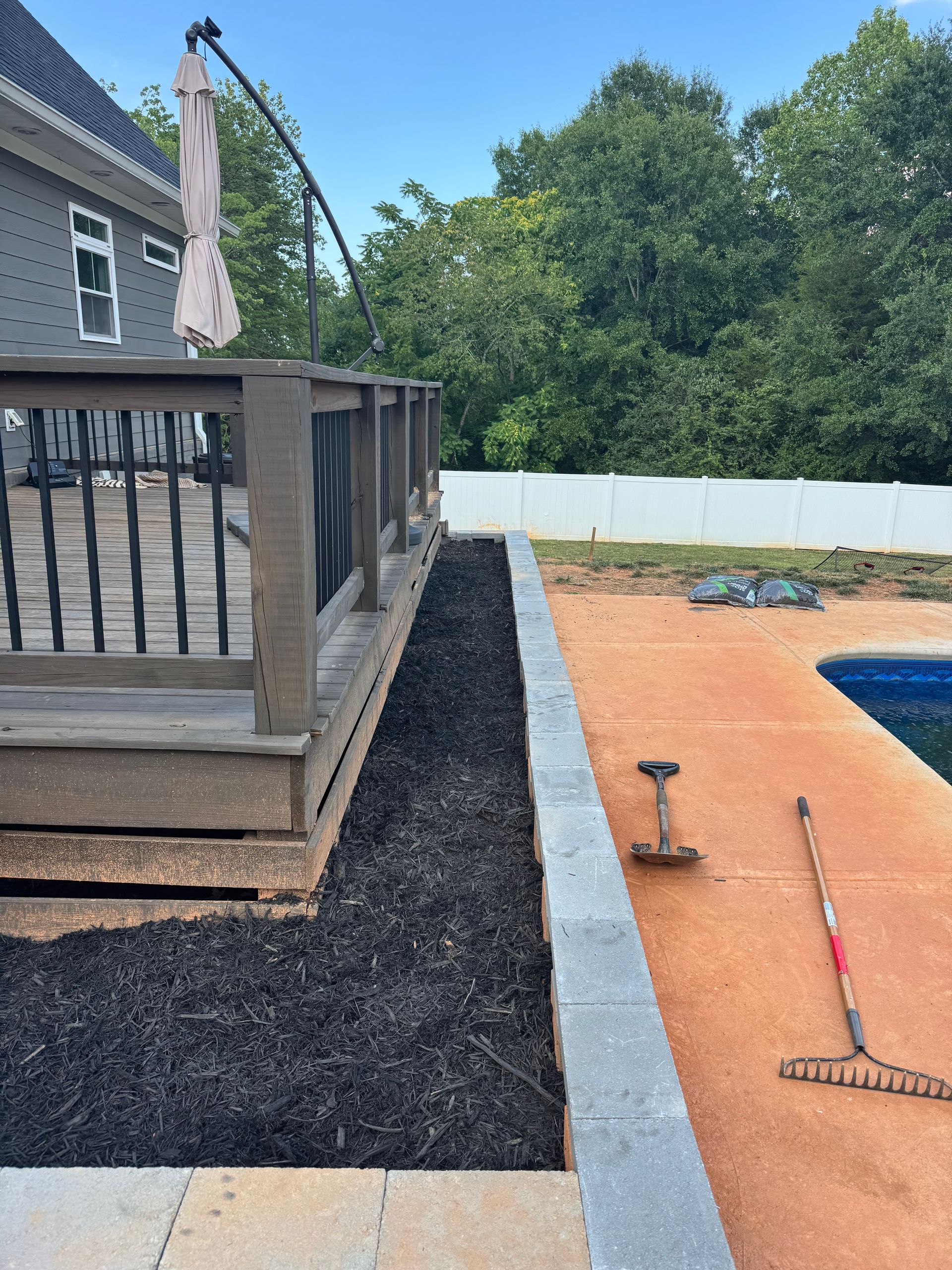 Backyard deck beside a gravel path and orange surface, with a pool and trees in the background
