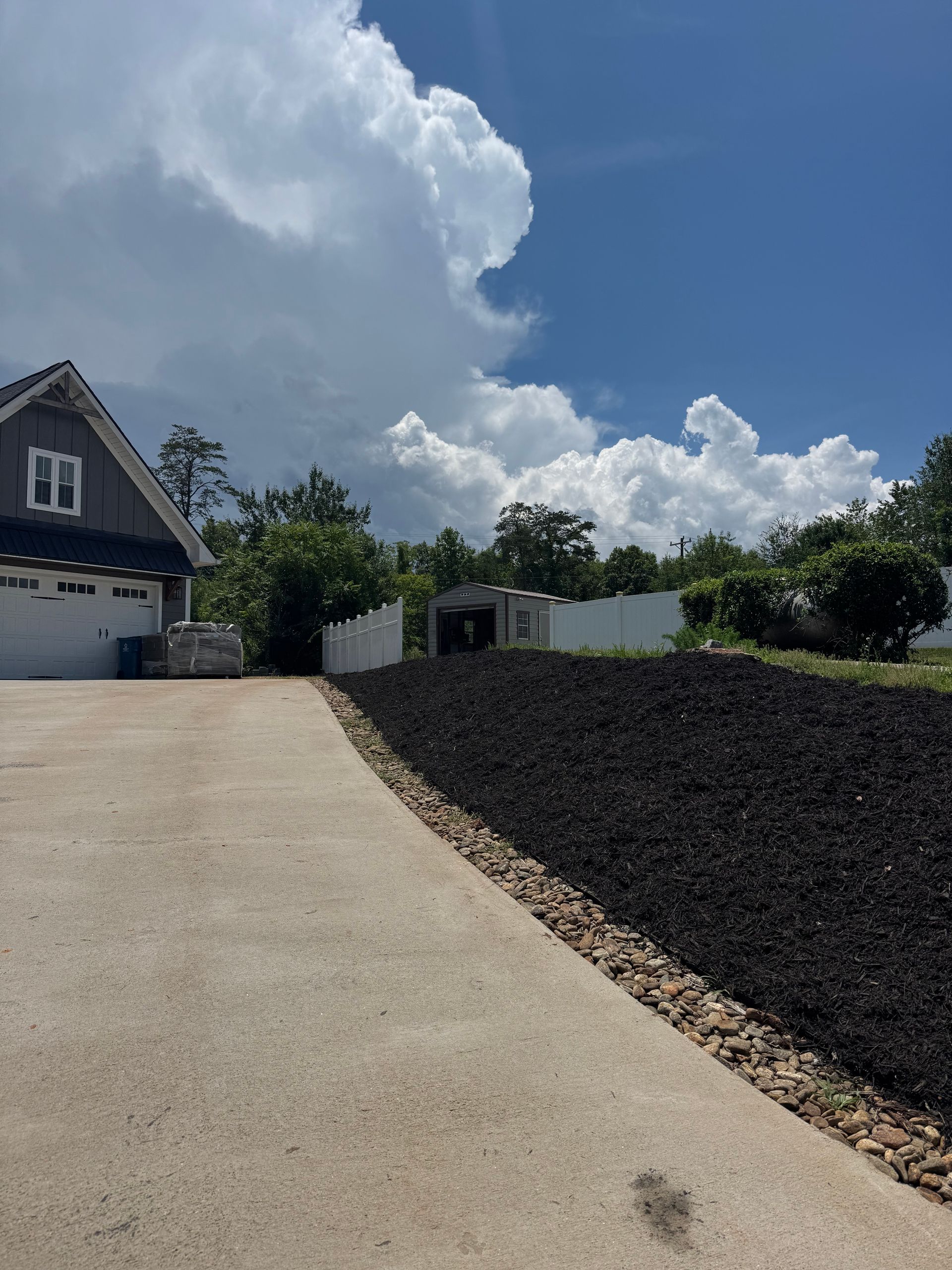 Steep concrete driveway leading to a house garage, with dark rock landscaping under a bright cloudy sky