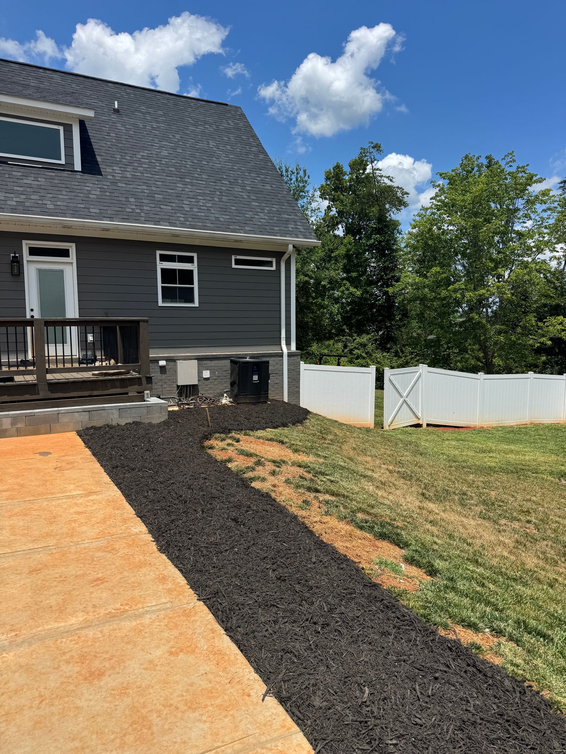 Backyard with gray house, black gravel path, and white fencing under a blue sky
